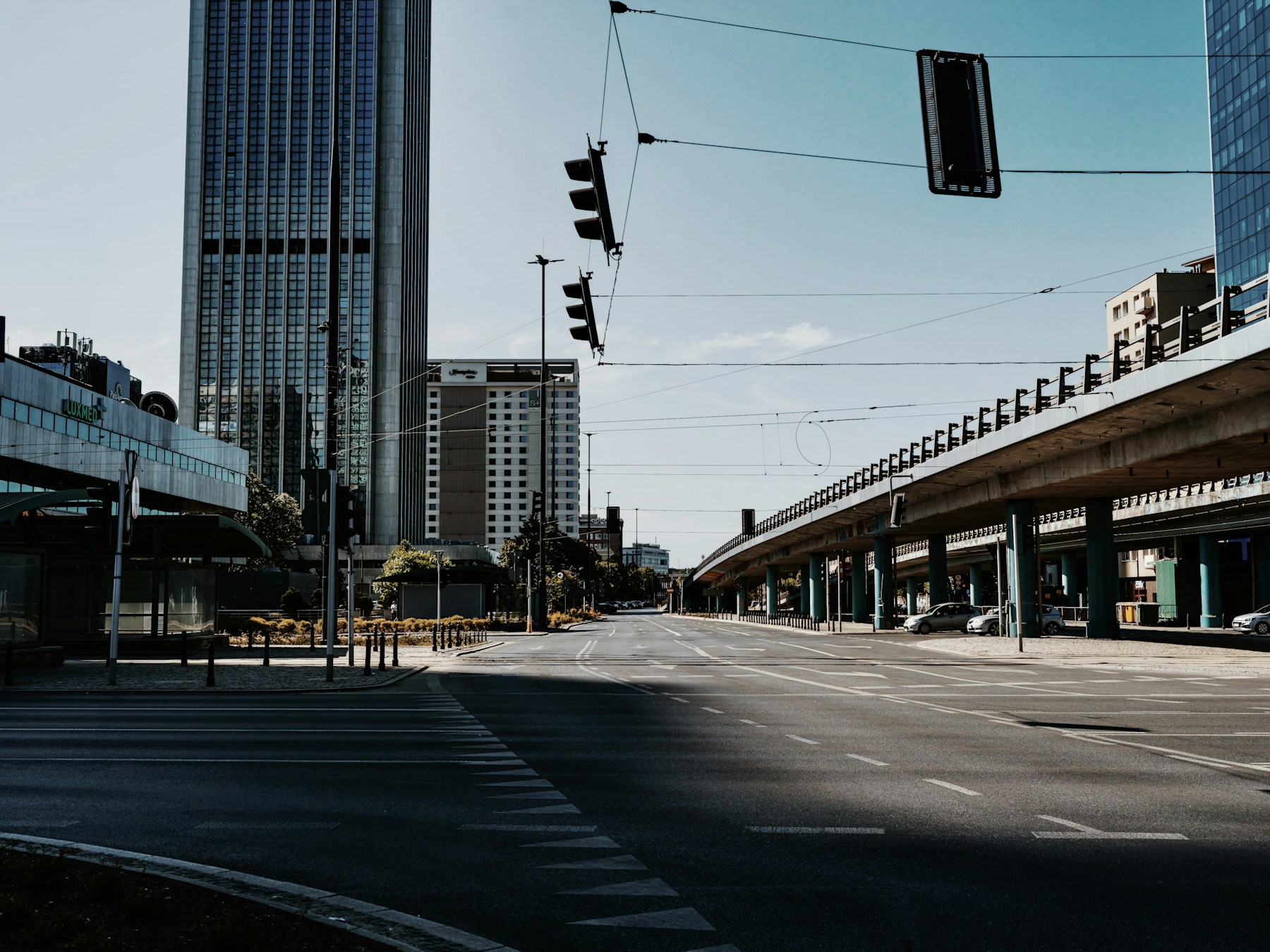 An empty Warsaw road beneath tram cables and elevated concrete