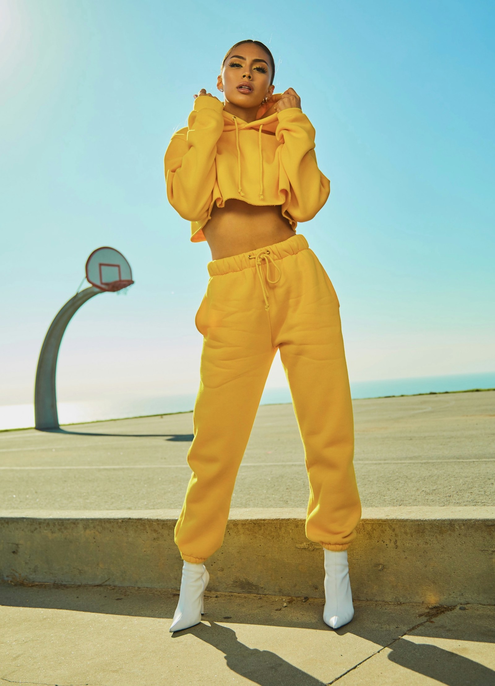 A woman in yellow standing in strong sun near a curved basketball hoop
