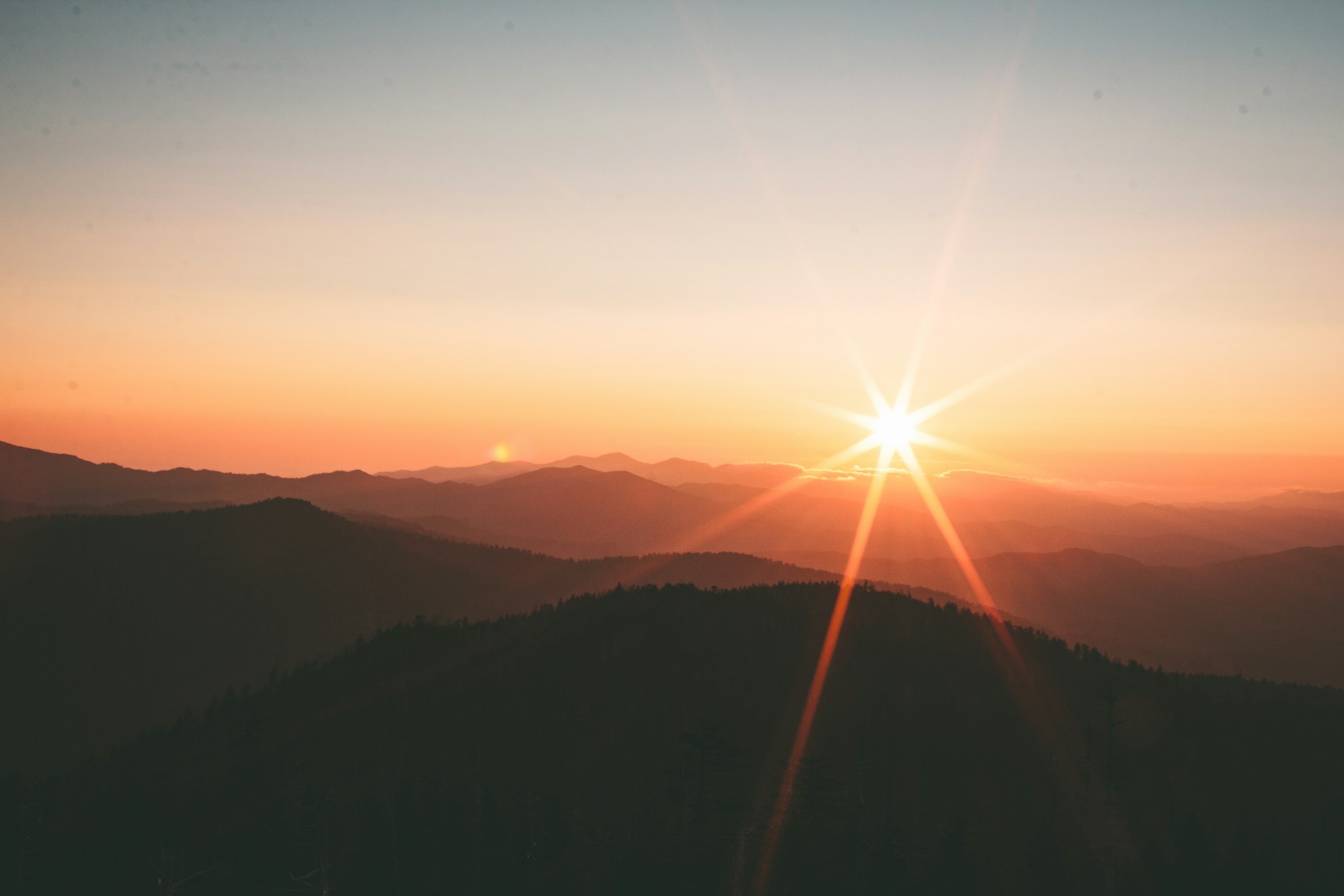 Layered mountain ridges under a low sun with a bright starburst